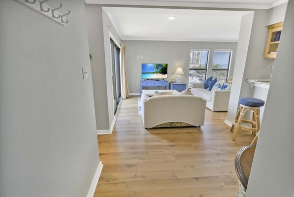 A modern living room with a sofa, a TV, and a dining area with a table and chairs. - 2BR Ocean Bridge - Shore Drive,Pool,Steps to Beach (Myrtle Beach)