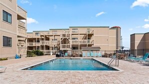 A swimming pool area with a brick patio, lounge chairs, and a multi-story building with balconies. - 2BR Ocean Bridge - Shore Drive,Pool,Steps to Beach (Myrtle Beach)
