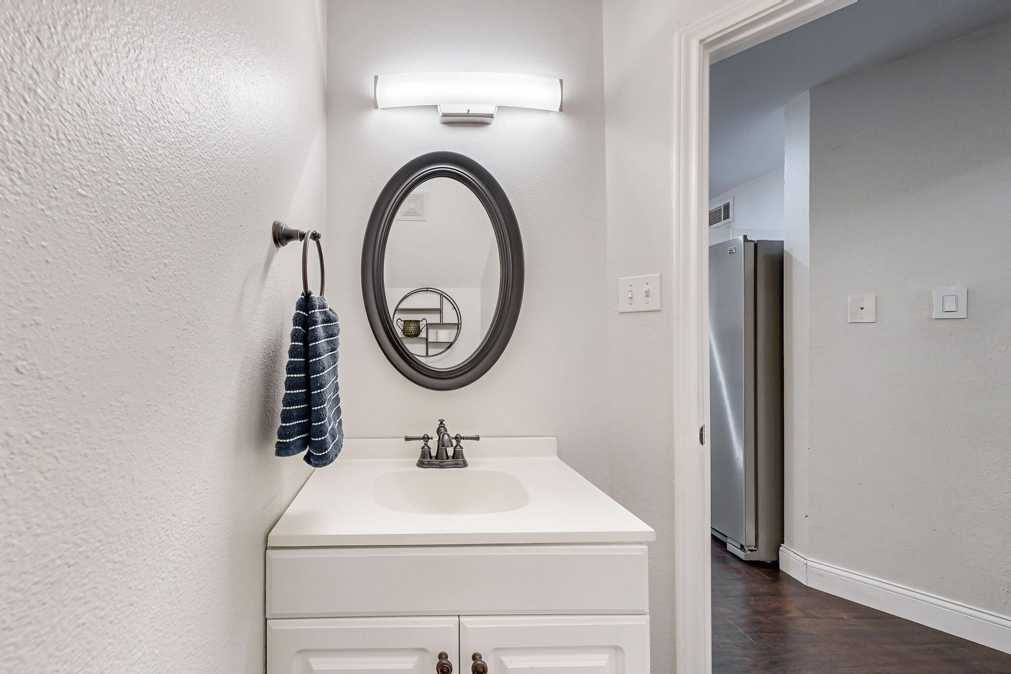 Une salle de bain avec un meuble-lavabo blanc, un miroir rond et un porte-serviettes.