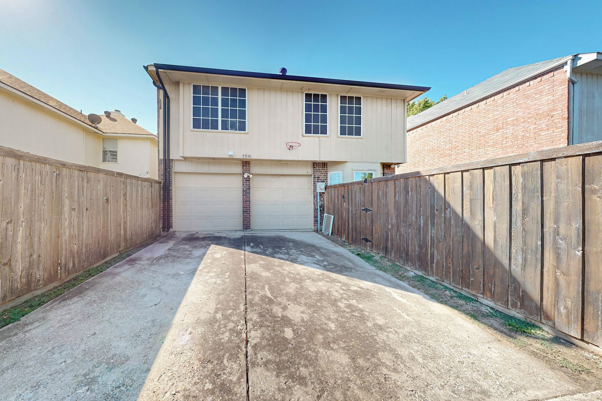 A two-story house with a garage, a basketball hoop, and a wooden fence.