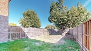 A fenced backyard with a grassy area, trees, and a brick building. - Charming 3-Bedroom Home in Prime Frisco Location Fast WiFi & AC (Frisco)