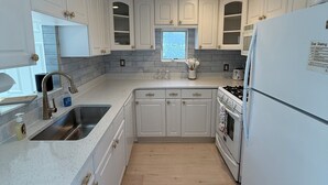 A kitchen with white cabinets, a stainless steel sink, a window, and a refrigerator.