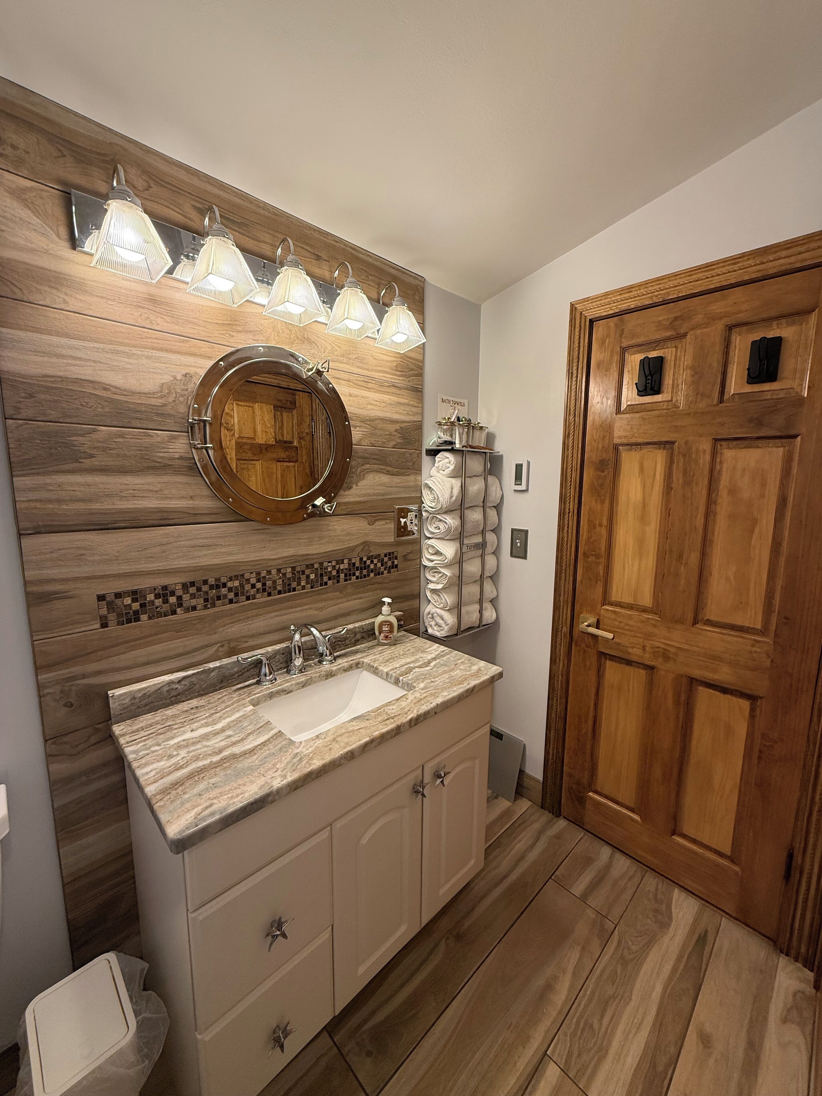 A bathroom with a wooden vanity, a round mirror, and a towel rack.