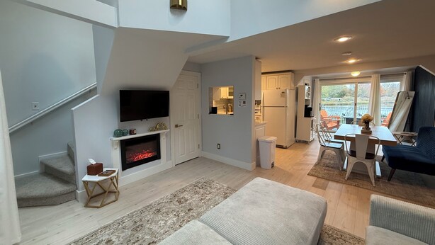 A spacious living area with a fireplace, a flat-screen TV, a dining table with chairs, and a large window offering a view of the outdoors.