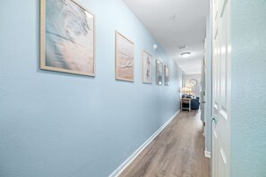 A hallway with light blue walls, wooden flooring, and framed artwork on the wall. - Grand Caribbean East Poolside Palms | Steps to Pools, Hot Tub, Beach | Garden Level & Lawn Area (Pensacola)