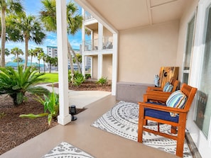 A covered outdoor seating area with a wooden bench, a patterned rug, and a view of a building with balconies.