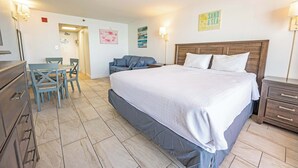 Ett hotellrum med en stor säng, ett skrivbord med en stol, en liten soffa och ett träbord som sängbord.