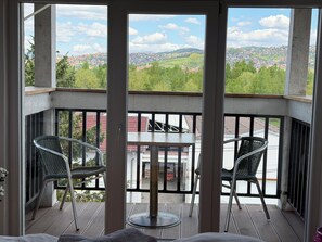 Un balcon avec deux chaises et une table, donnant sur un quartier résidentiel avec des maisons et de la verdure.