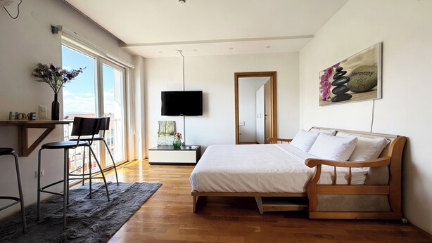 Une chambre moderne avec un lit en bois, un bureau avec une chaise, une télévision et une grande fenêtre.
