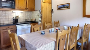 A compact kitchen with wooden cabinets, a microwave, a sink, and a dining table with chairs. - Duplex for 8, Quiet, Near Shuttle and Pool (Aussois)