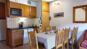 A compact kitchen with wooden cabinets, a microwave, and a dishwasher. There is a dining table with chairs and a small table lamp. - Duplex for 8, Quiet, Near Shuttle and Pool (Aussois)