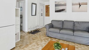 Un soggiorno con un divano grigio, un tavolino in legno, un frigorifero bianco e una porta che dà su un bagno.