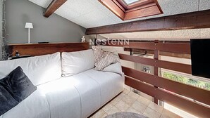 A bedroom with a sloped ceiling, a skylight, a white sofa, and a wooden headboard.