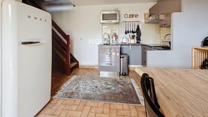 A compact kitchen with a white refrigerator, wooden staircase, and a kitchen island with hanging utensils.