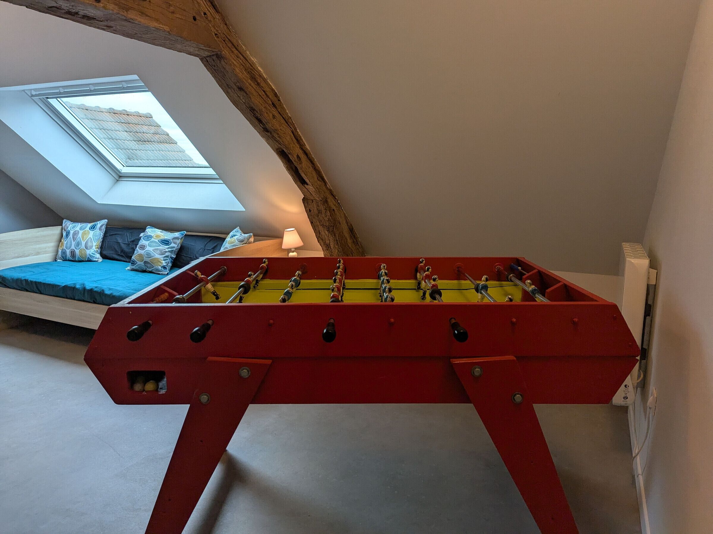 A room with a foosball table, a lofted sleeping area with a skylight, and a radiator.
