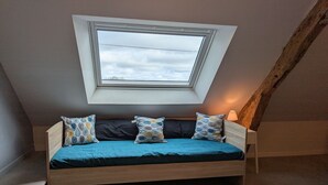 Une chambre à coucher aménagée dans un espace de type « loft », avec une lucarne, un lit en bois et des coussins à motifs.