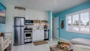Una cocina compacta con armarios blancos, electrodomésticos de acero inoxidable y una pared de acento color verde azulado.