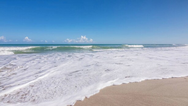 Una playa con olas acercándose a la orilla, cielo despejado y arena.