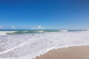A beach with waves approaching the shore, a clear sky, and a sandy beach. - Castaway Cottage – paradise at the beach! (Indialantic)