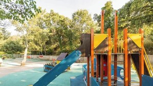 Une aire de jeux avec un toboggan bleu, des structures d’escalade orange et une cabane de jeu jaune.