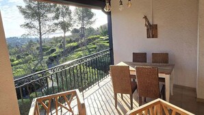 Un espace extérieur aménagé, abrité et doté de mobilier en osier, d’une petite table ornée d’une plante en pot et offrant une vue sur un jardin paysager.