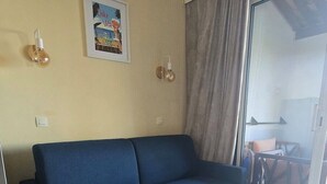 Un salon avec un canapé bleu, une table basse ronde blanche et un tapis à motifs.