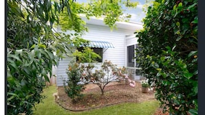 Un patio trasero residencial con una casa blanca, un árbol pequeño y un césped bien cuidado.