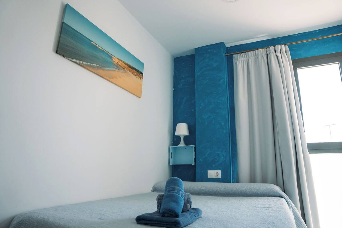Quarto com cama, um quadro, mesa de cabeceira com abajur e janela com cortinas.