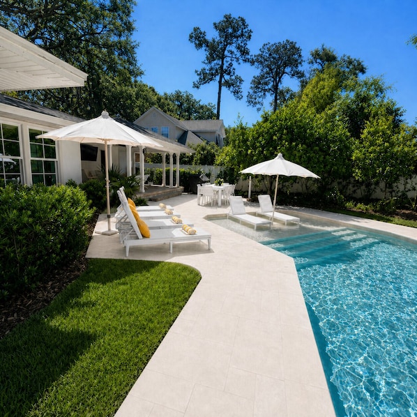 A poolside area with lounge chairs, umbrellas, and a clear blue pool.
