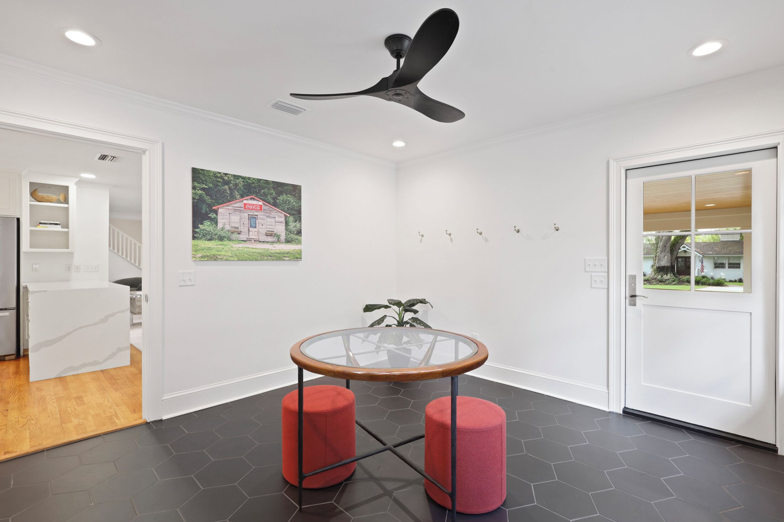 A modern room with a glass-top table, two red stools, a ceiling fan, and a door leading to another room.