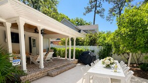 A covered patio with a dining table and chairs, a barbecue grill, and a small outdoor seating area. - The Maggie Mae: Stylish Retreat | Private Pool + Walk to the Best of St. Simons (Saint Simons Island)