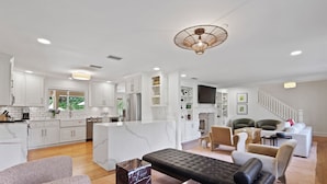 A spacious living area with a modern kitchen, a dining area, and a seating area with a sofa and chairs. - The Maggie Mae: Stylish Retreat | Private Pool + Walk to the Best of St. Simons (Saint Simons Island)