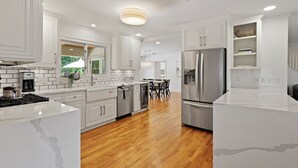 A modern kitchen with white cabinetry, stainless steel appliances, and a wooden floor. - The Maggie Mae: Stylish Retreat | Private Pool + Walk to the Best of St. Simons (Saint Simons Island)