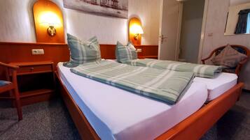 Una camera d'albergo con un letto di legno, due lampade sui comodini, un quadro appeso al muro e una poltrona con cuscino.