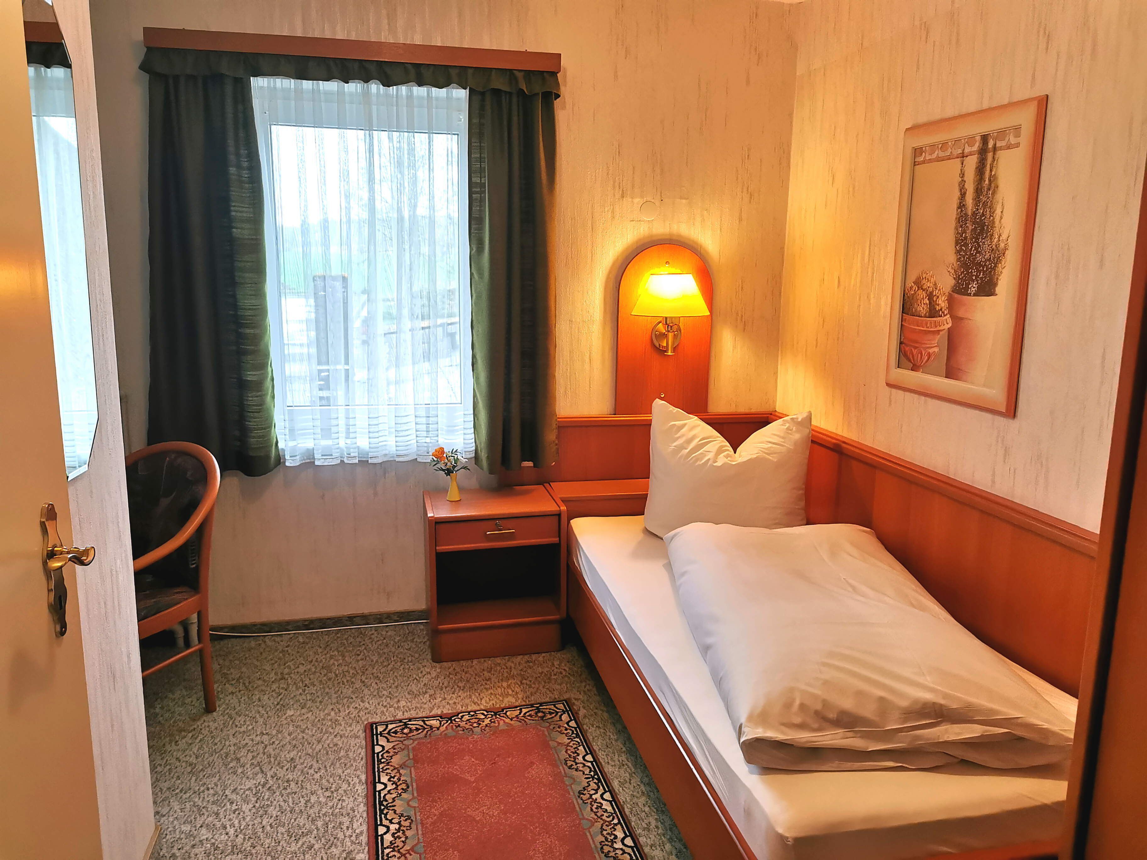 A hotel room with a bed, a nightstand, a lamp, a chair, and a window with curtains.