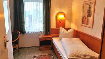A hotel room with a bed, a nightstand, a lamp, a chair, and a window with curtains.