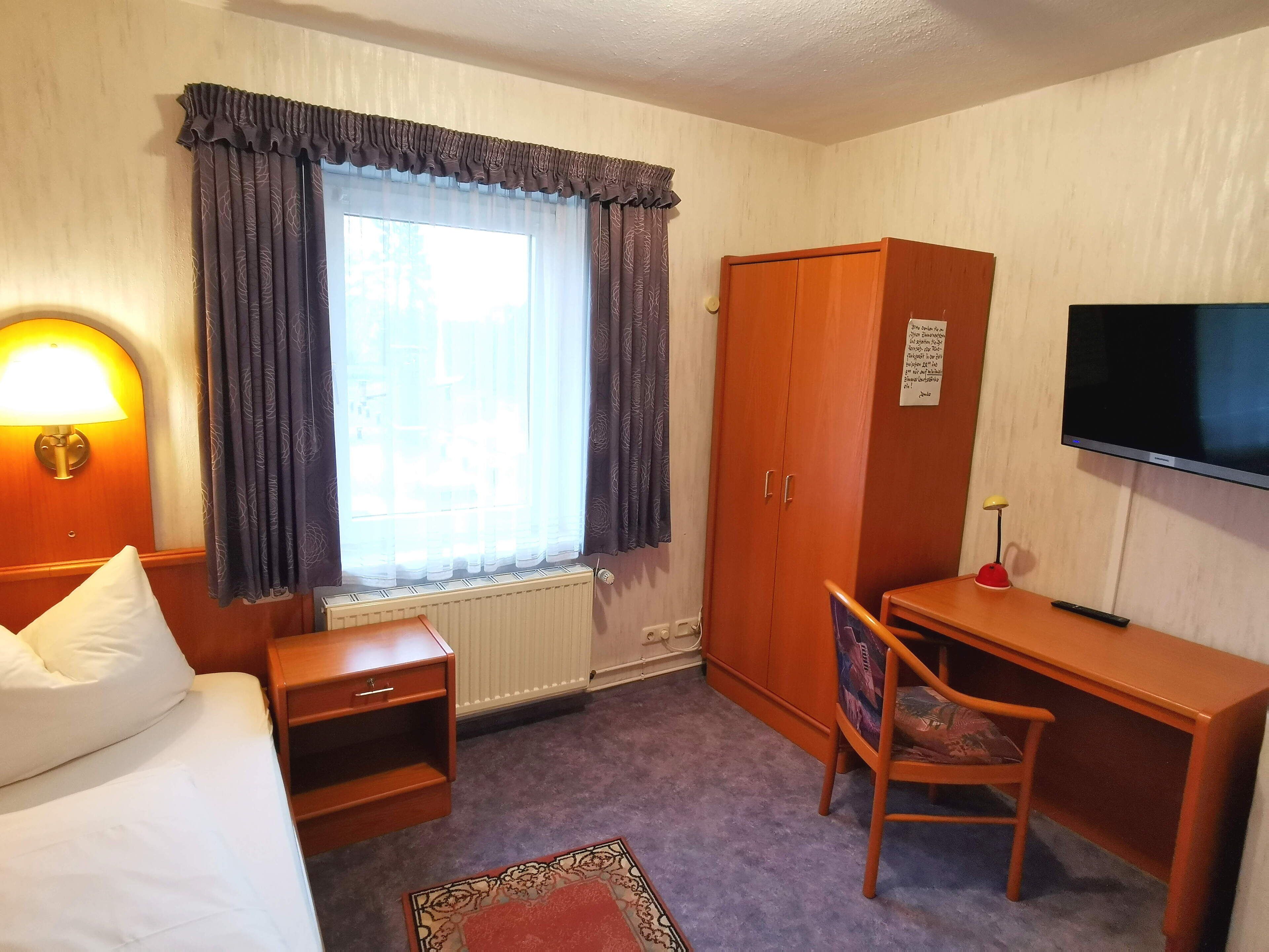 Una habitación de hotel con cama, escritorio, silla, televisión y armario.
