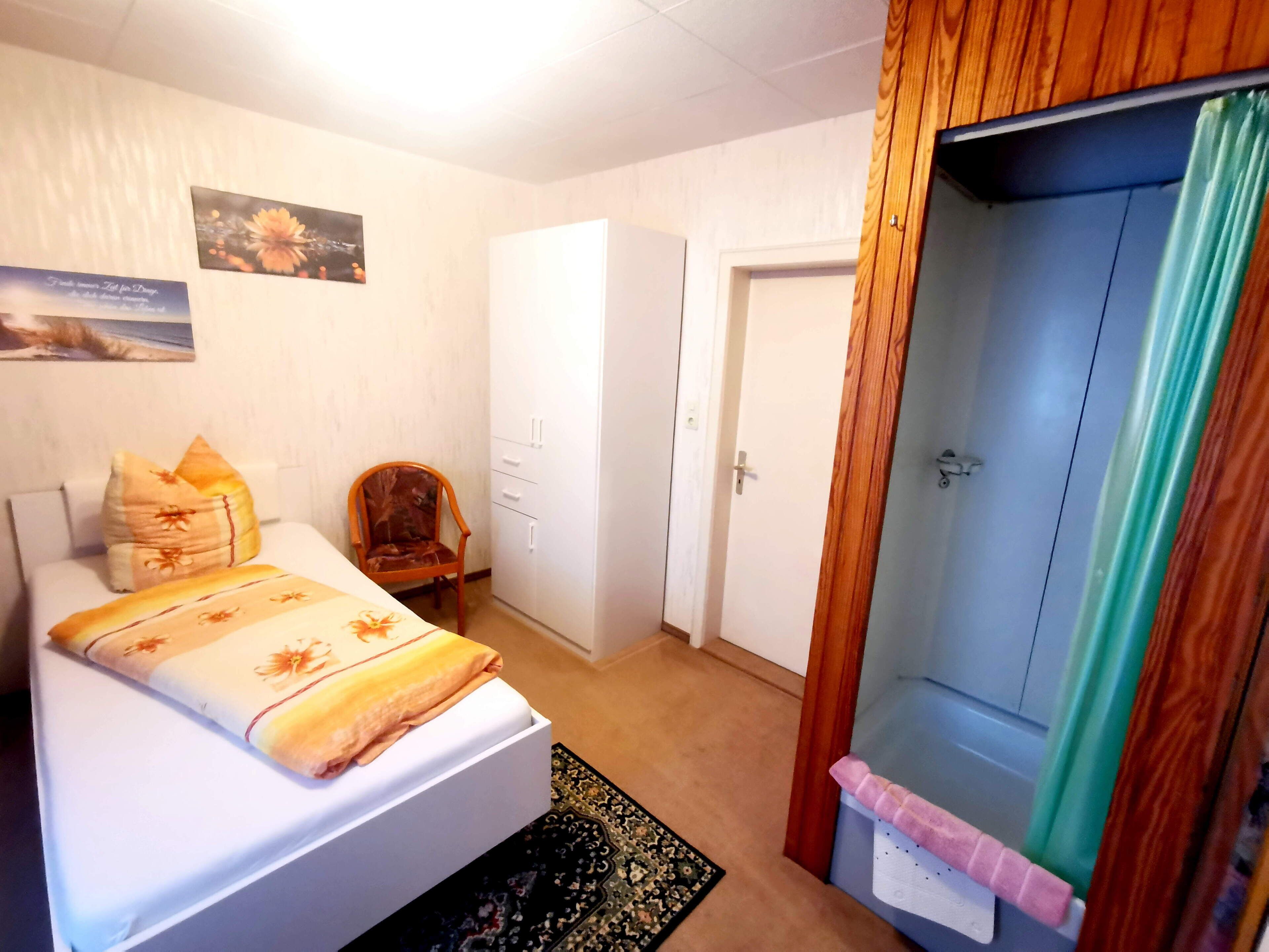 A bedroom with a bed, a chair, a wardrobe, and a door.