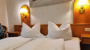 Habitación de hotel con cama doble, dos almohadas blancas, cabecera de madera y dos lámparas fijadas a la pared.