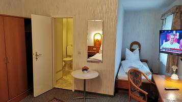 Habitación de hotel con cama, televisión, mesita, silla, escritorio, espejo y armario.