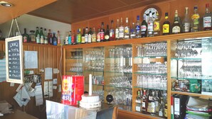Zona de bar con estantes llenos de botellas de licor y una vitrina de vidrio con distintos vasos.