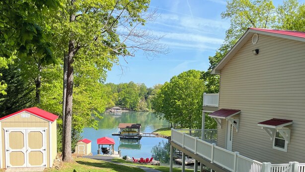 Une propriété au bord du lac, dotée d’un quai couvert, d’un petit abri de jardin et d’une maison avec un toit rouge et une façade blanche.