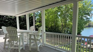 Une terrasse couverte, dotée de chaises Adirondack et d’une table, avec vue sur un lac.