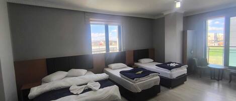 Habitación de hotel con tres camas, ventanas amplias y un balcón.