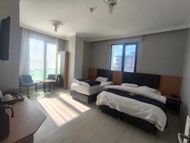 Habitación de hotel con dos camas, un escritorio, una silla y ventana con vistas a edificios.