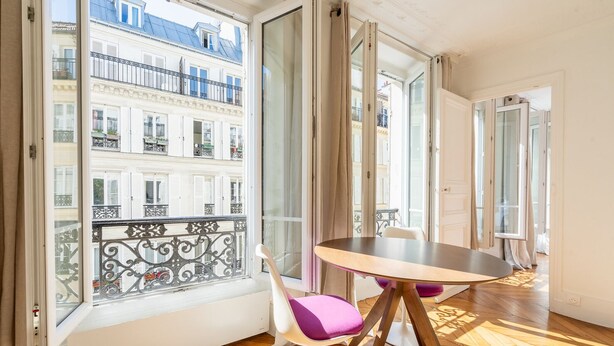 A balcony with a view of Parisian buildings, a round table with chairs, and a wooden floor.