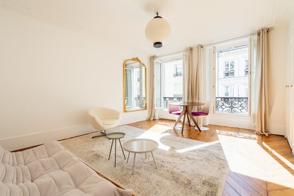 A spacious living room with a sofa, two chairs, a small table, and a large window with a view of buildings.