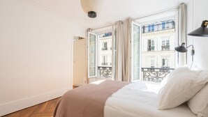 A bedroom with a bed, a bedside lamp, and a view of a balcony with railings.