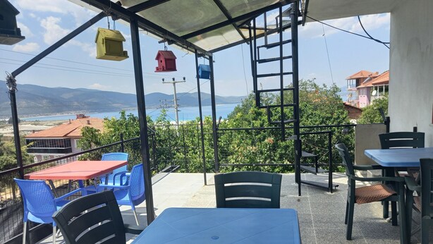 A terrace with a table and chairs, overlooking a scenic view of a body of water and hills. - Tan Apart Aile Ev Pansiyonu (Yesilova)