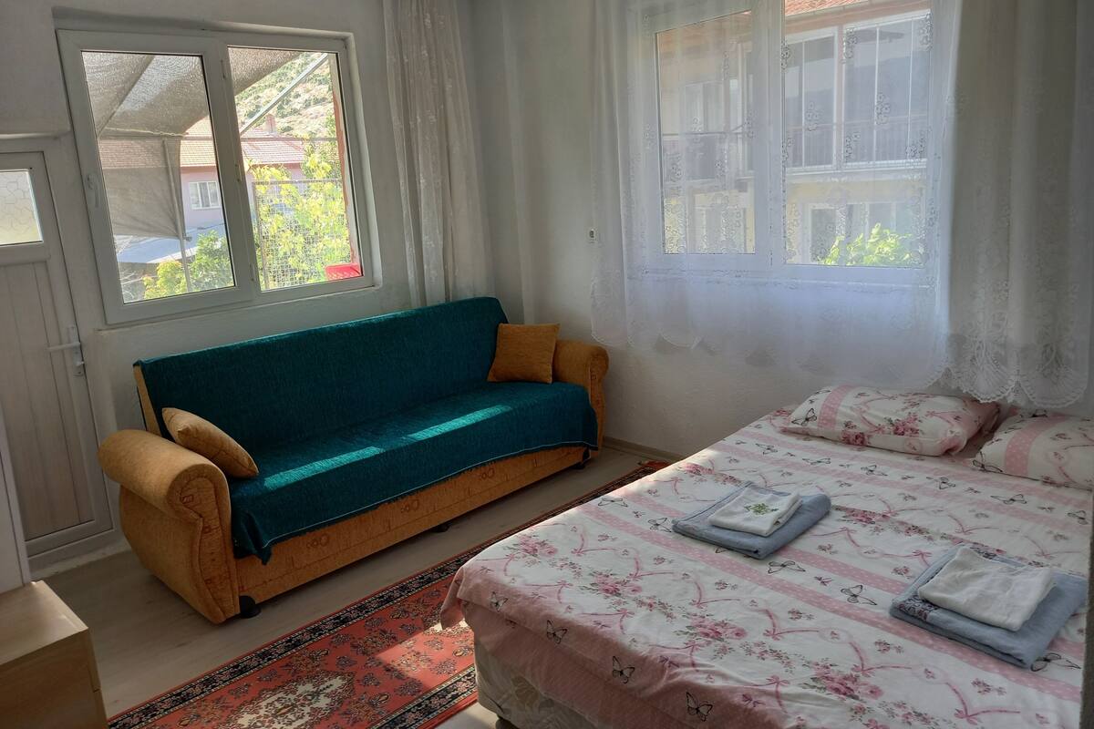 Un dormitorio con sofá, cama con ropa de cama floral, ventana con cortinas y vistas al exterior.